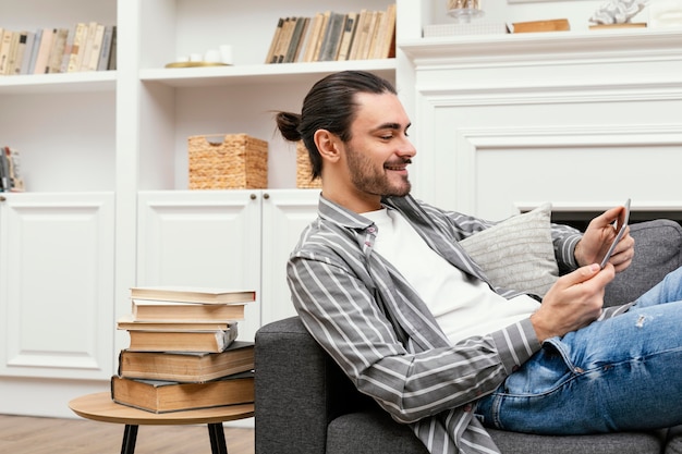 Uomo di vista laterale che si siede sul divano con un tablet