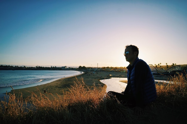 Side view of man sitting on shore against clear sky