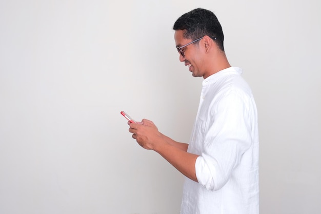 Photo side view of a man smiling while texting on his mobile phone