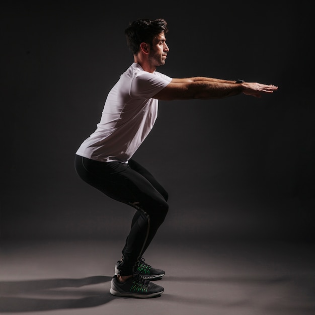 Photo side view man squatting on dark background