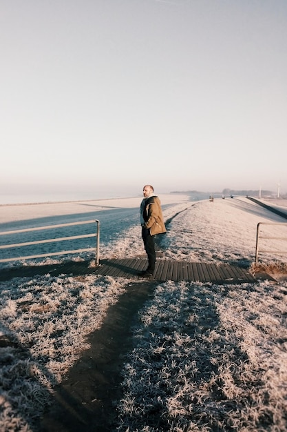 Side view of man standing on beach against clear sky during winter