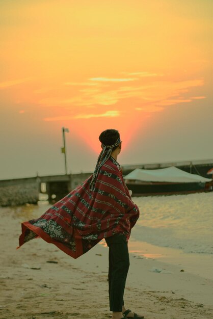 Side view of man standing at beach during sunset