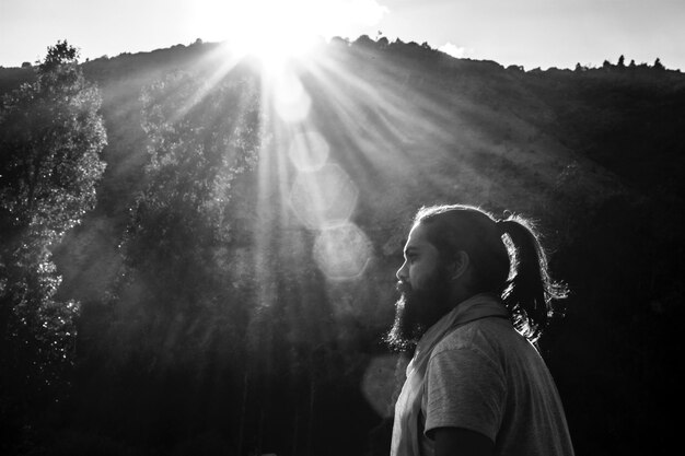 Photo side view of man standing in forest during sunny day