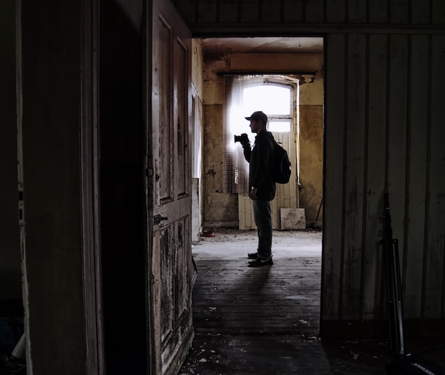 side view of man standing with camera in abandoned house