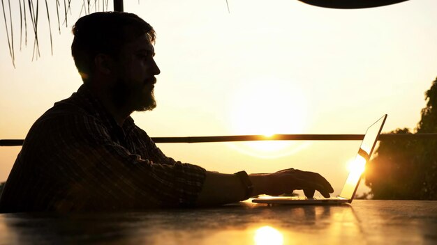 Photo side view of man using laptop on table against sky during sunset