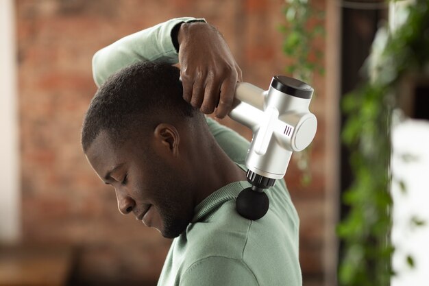 Photo side view man using massage gun for shoulder pain