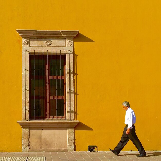 Side view of man walking on road against yellow building