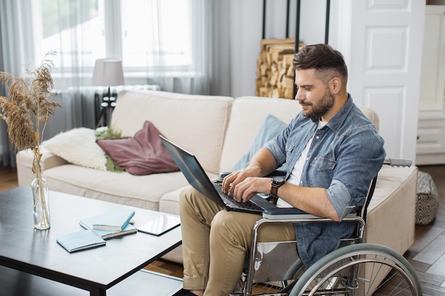 Side view of man in wheelchair typing on laptop indoors