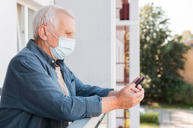 Photo side view man with phone wearing mask