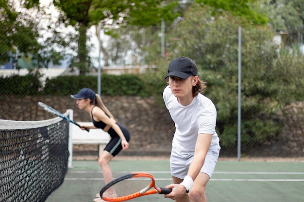 ボールを打つことを試みているネットの近くで試合をすることに集中している男女のテニスカップルの側面図