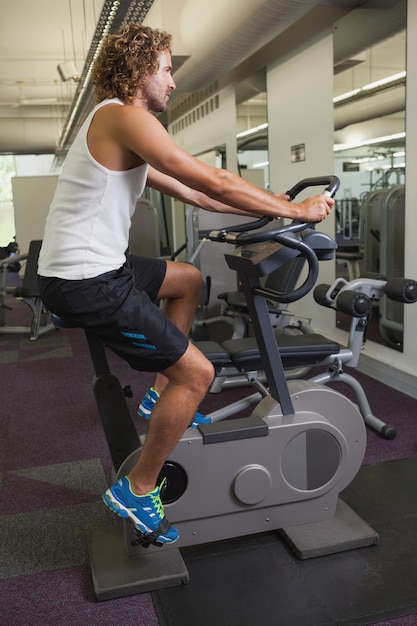 Foto vista laterale dell'uomo che risolve sulla bici di esercizio alla palestra