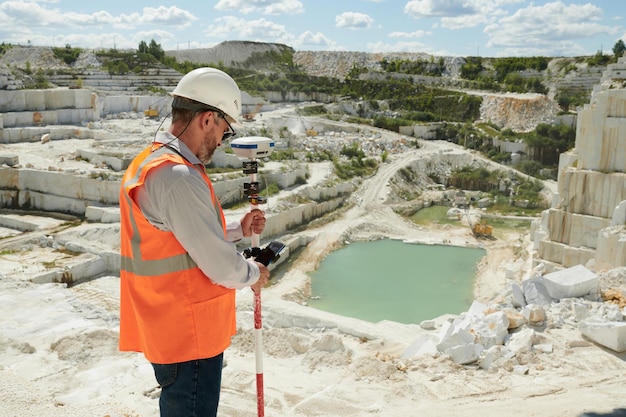 Vista laterale dell'ingegnere maturo o del geometra che regola il teodolite prima del lavoro