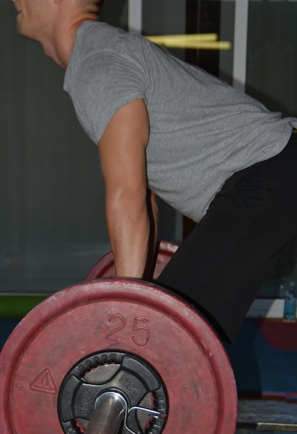 Photo side view of mid adult man lifting weights in gym