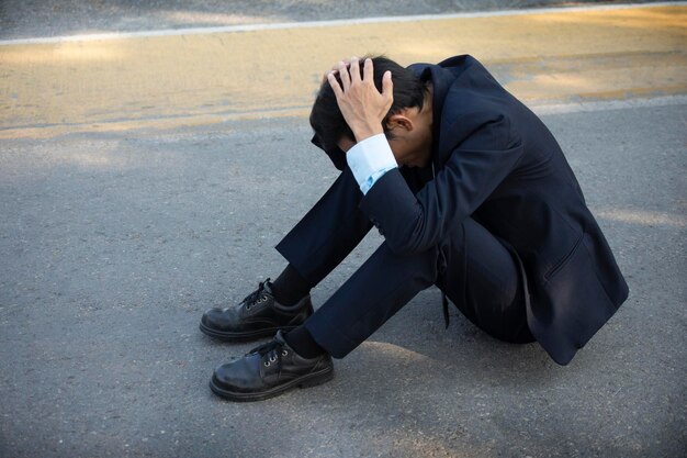 Side view of mid adult man with head in hands sitting on road