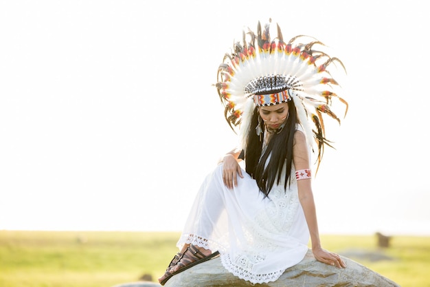 Photo side view of mid adult woman in traditional clothing sitting on rock against sky