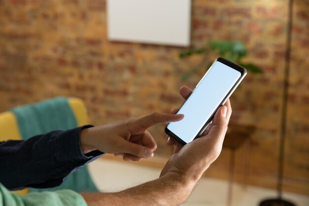 Photo side view mid section of a young caucasian couple using a smartphone in their sitting room, the man holding it and the woman touching the screen