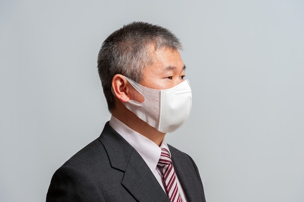 Side view of middle aged Asian man with suit and tie wearing white surgical mask