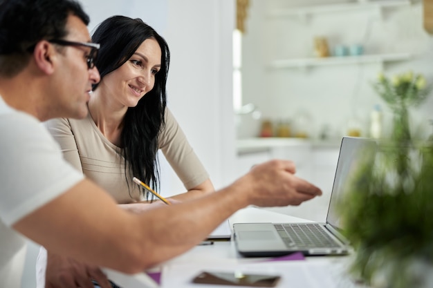 Vista laterale della coppia latina di mezza età, uomo e donna che comunicano durante il corso di formazione online mentre studiano a distanza, utilizzando il laptop a casa. formazione a distanza per adulti