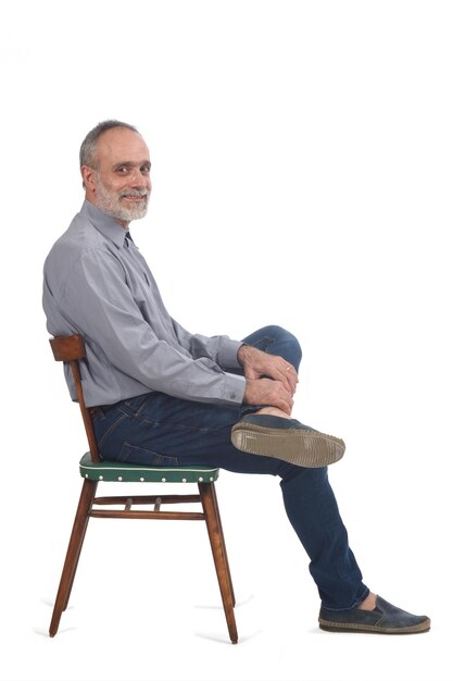 흰색 배경에 있는 카메라를 바라보며 의자에 앉아 있는 중년 남성의 측면