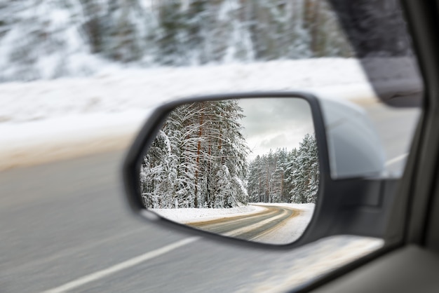 Side view mirror reflection of Snow-covered road in forest