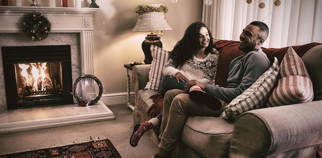 Side view of a mixed race couple in their sitting room at Christmas, sitting on a sofa talking and smiling