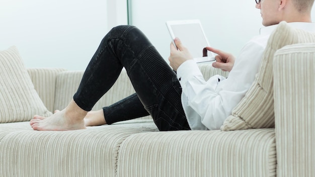 Side view modern guy reading an ebook sitting on the couch of his living room