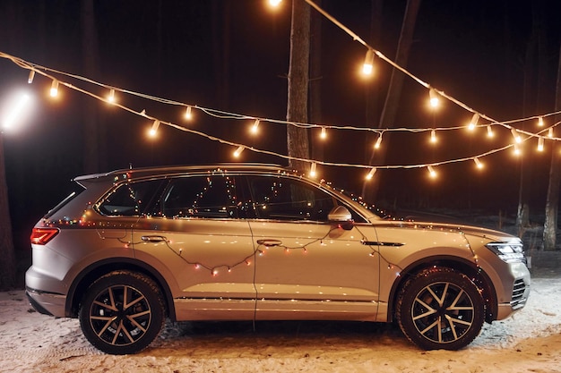 Side view Modern silver colored automobile parked in forest with holiday decoration