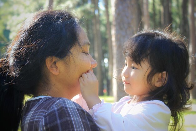 Photo side view of mother and daughter against trees