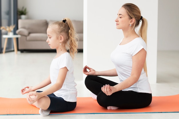 side view of mother and daughter doing a yoga pose at home
