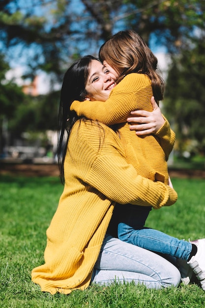 Photo side view of mother embracing daughter while kneeling on grassy field in park