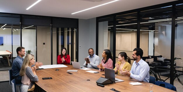 Side view of a multi-ethnic group of men and women sitting together by a table in the meeting room, discussing and interacting.