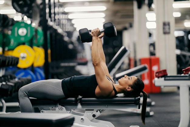 Side view of a muscular sportswoman lying on a bench in a gym and doing exercises for biceps