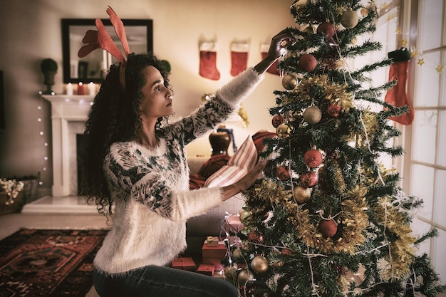 写真 クリスマスに彼女の居間で混血の女性の側面図、ひざまずいて、お祝いの帽子をかぶって、クリスマス ツリーを飾る