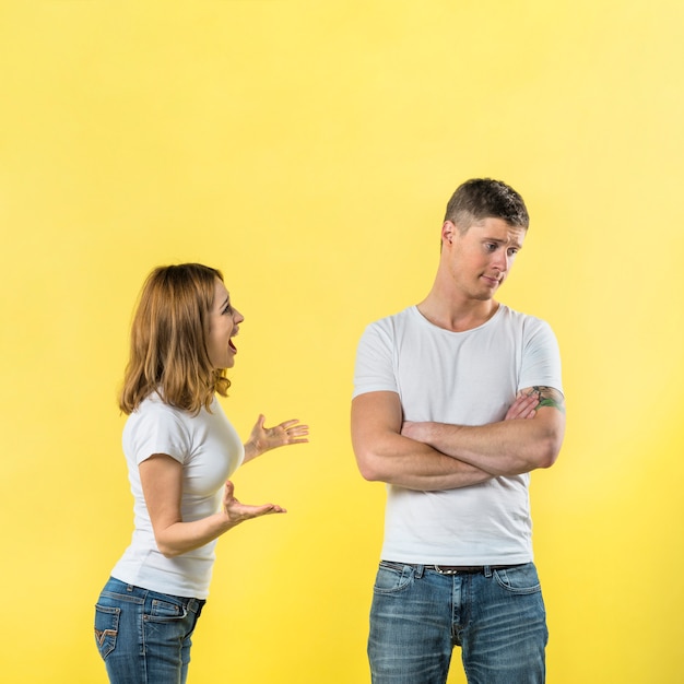 Вид сбоку молодой женщины ругает своего парня на желтом фоне