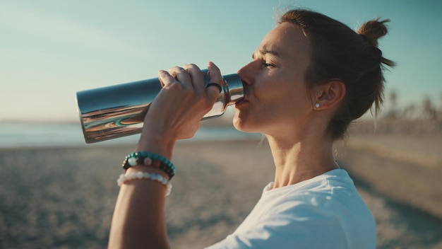 写真 ビーチで朝のヨガの後に休んでいる美しいブロンドの女性の飲料水の側面図