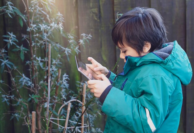 写真 デジタルタブレットを使用している少年が屋外の植物の横から見える