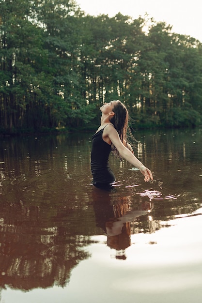 사진 옷 을 입은 무관심 한 여자 가 호수 의 조용 한 물 에 서서 여름 에 자유 를 즐기고 있는 측면 광경