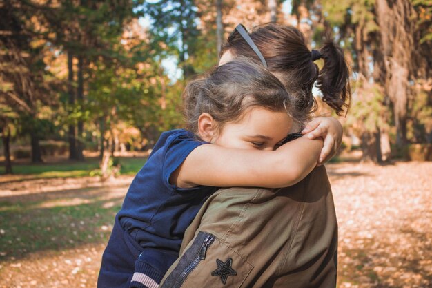 写真 秋の公園で母親を抱きしめる女の子の横の景色