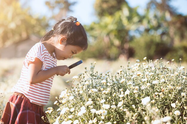 写真 公園で拡大鏡で花を見ている女の子のサイドビュー