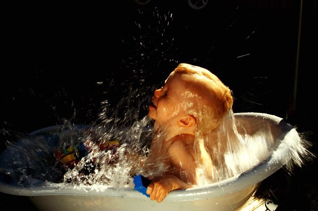 写真 浴槽で水を噴くシャツを着ていない男の子のサイドビュー