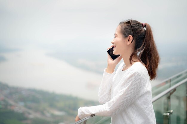 写真 笑顔の若い女性がスマートフォンに応答しながら風景に逆らっている横の景色