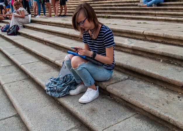 写真 階段に座って携帯電話を使っている十代の女の子の横の景色