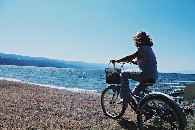 写真 晴れた日に空に照らして海で自転車に乗っている女性の横景色