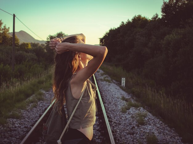 写真 空に向かって鉄道線路に立っている女性のサイドビュー
