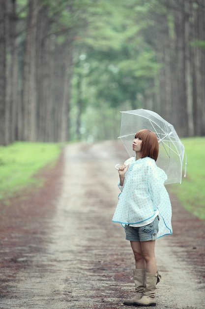 写真 森の木の反対側の道路に立っている傘をかぶった女性のサイドビュー