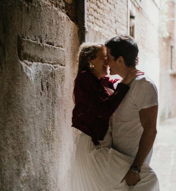 写真 壁に寄りかかってキスしている若いカップルの横の景色