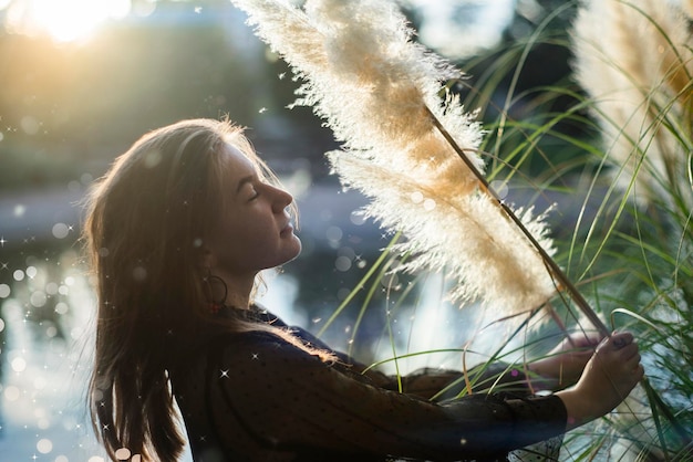 写真 野外で植物を抱いている若い女性の横の景色