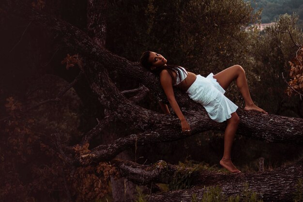 Фото Боковой вид молодой женщины, лежащей на стволе дерева в лесу