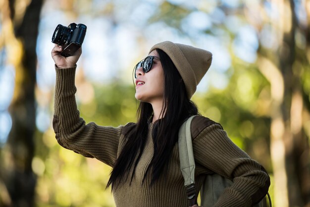 写真 森に立ってカメラで写真を撮っている若い女性の横の景色