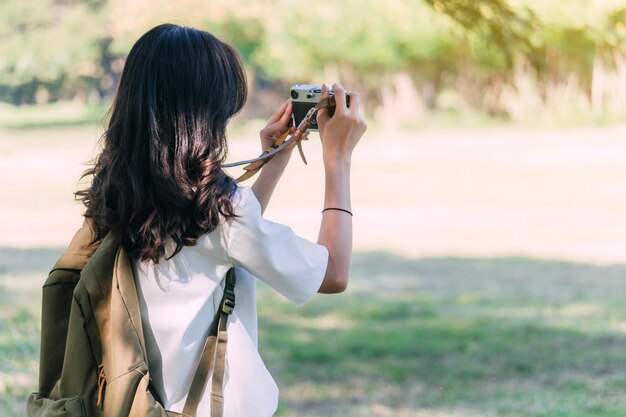写真 公園に立っている間にバックパックを背負って写真を撮っている若い女性のサイドビュー